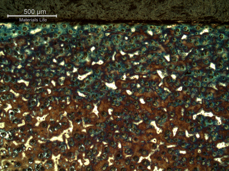 Micrography of the shaft at the surface, in a heat treated position.  Graphite in nodules. Dark blue martensitic microstructure around the nodules and white islands of martensitic with retained austenite microstructure (not clearly identified at this low magnification).