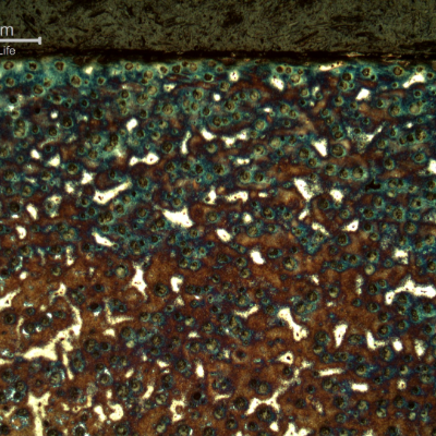 Micrography of the shaft at the surface, in a heat treated position.  Graphite in nodules. Dark blue martensitic microstructure around the nodules and white islands of martensitic with retained austenite microstructure (not clearly identified at this low magnification).