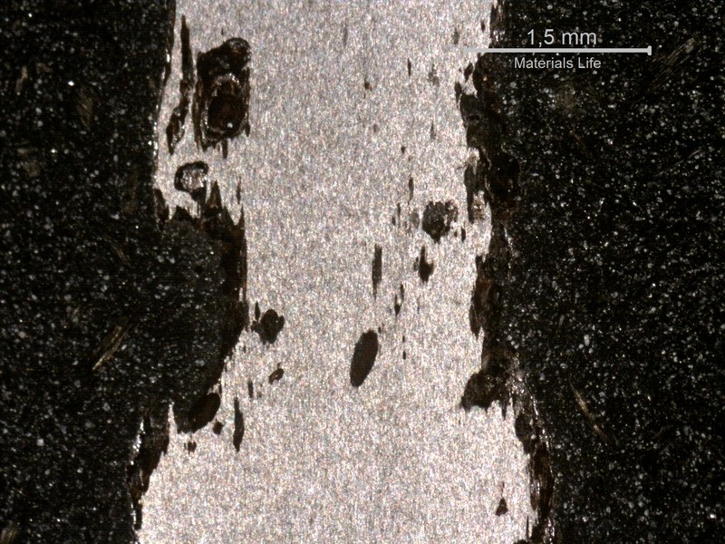 Cross-sectional view of a wire showing irregular corrosion pits penetrating inward from both surfaces.
