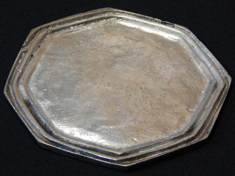 Piece that was analysed by non destructive tests.  Octogonal shape. Two irregular grooves.  The coaster was manufactured in a cooper alloy substrate and a metallic coating. The analysis to reveal the substrate microstructure was conducted on the back of the part, in a non destructive preparation, that included light grinding, polishing and etching.