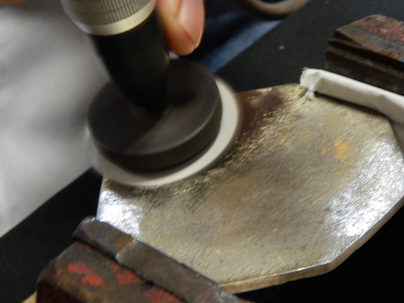 Light grinding the back of the coaster.  The surface was only partially ground, removing the metallic coating, and exposing the substrate, that appeared yellow indicating the manufacturing in a cooper alloy.