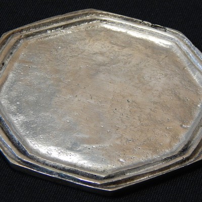 Piece that was analysed by non destructive tests.  Octogonal shape. Two irregular grooves.  The coaster was manufactured in a cooper alloy substrate and a metallic coating. The analysis to reveal the substrate microstructure was conducted on the back of the part, in a non destructive preparation, that included light grinding, polishing and etching.