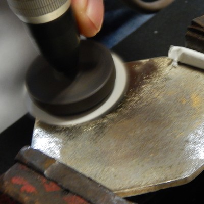 Light grinding the back of the coaster.  The surface was only partially ground, removing the metallic coating, and exposing the substrate, that appeared yellow indicating the manufacturing in a cooper alloy.