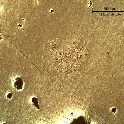 Metallographic aspect of the polished surface of the (back of the) coaster, showing pores and shrinkages, typical of a casting structure.