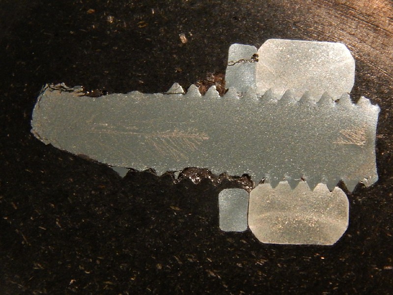 Macrography of the longitudinal section of a fractured bolt, still threaded to the nut and with the lock washer. The cracks can be seen in several positions: in the threads (removing then); in the center of the bolt (branched) and also in the washer (longitudinal branched cracks).