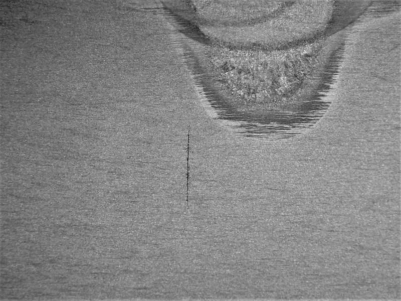 Macrographic detail of the longitudinal section of the valve body, at the cracked position, a little far from the actuator hole.  There is a straight crack, transverse to the thickness that clearly propagated by fatigue mechanism, from the region where the welding defects were created.