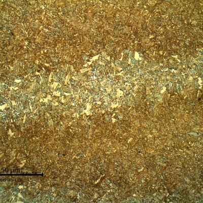 Micrography of a longitudinal section of the valve body presenting a martensitic microstructure.  The structure is banded and the darker regions show inclusions (grey sulfides).