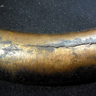 Macro view of a bent tube section showing a transverse surface crack with dark staining along the crack path on the outer bend.