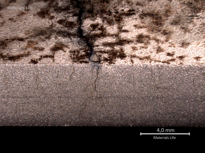 Macrographic detail of the longitudinal section of the stub end, showing the external side to the top and the internal side to the bottom. There are multiple cracks starting from the external side.