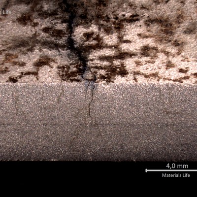 Macrographic detail of the longitudinal section of the stub end, showing the external side to the top and the internal side to the bottom. There are multiple cracks starting from the external side.