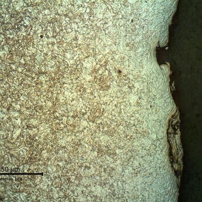 Micrography of a longitudinal section of the pipe, at the internal pipe surface,  where the coating was detached.  The strain hardening effect of the blasting is evident. The microstructure is tempered martensite and the surface is slightly decarburized.