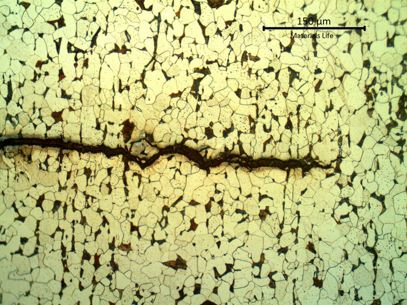 Etched micrograph showing a transgranular crack running across equiaxed ferrite grains with dark grain-boundary carbides.