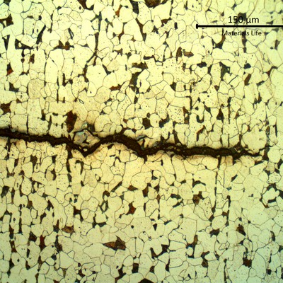 Etched micrograph showing a transgranular crack running across equiaxed ferrite grains with dark grain-boundary carbides.