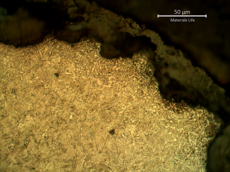 Micrographic detail of spring surface, showing the pits full of corrosion deposits and a small decarburized layer (probably from the manufacturing processes).