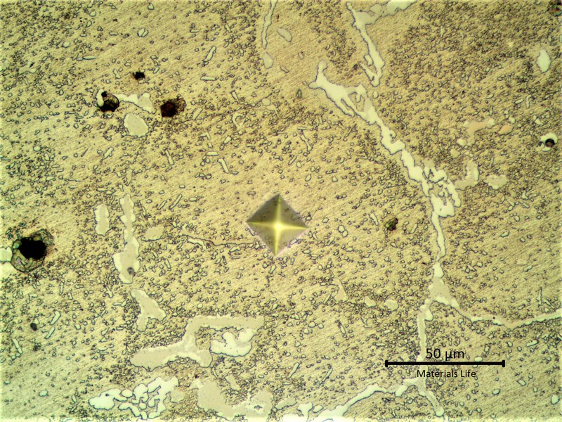 Aged microstructure of the HP stainless steel, modified with 1%Nb, cast fitting, tubular, operating for 6 years in a furnace which design temperature is 1100°C.  The material presented a network of primary carbides, white and grey, and an austenitic matrix with coalescing secondary precipitation. Some voids. The Vickers identation indicates a hardness value about 260HV 100g in the aged austenitic matrix.