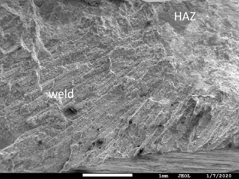 The fracture surface in the sample shows columnar grains in the weld and large facets in the heat affected zone (HAZ) close to the internal surface of the carcass (to the top of the image).