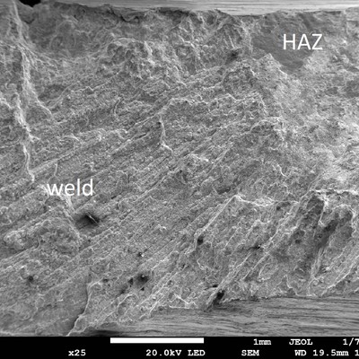 The fracture surface in the sample shows columnar grains in the weld and large facets in the heat affected zone (HAZ) close to the internal surface of the carcass (to the top of the image).