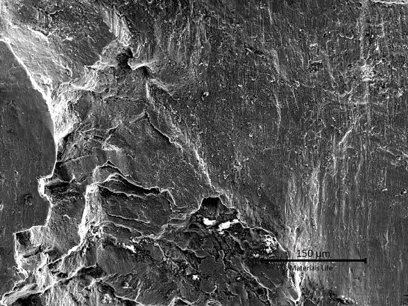 Low magnification image by scanning electron microscopy.  In the bottom of the image the fracture appearance is brittle and presenting several secondary cracks.  In the top  of the image the fracture is fully flat, also without macroscopic plastic deformation.