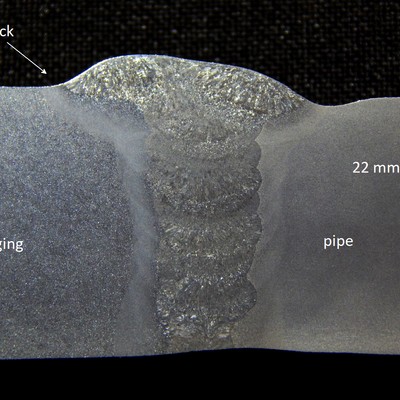 Macrography of the welded joint between the forging and the pipe, showing it was welded in a narrow gap, indicating by the arrow the location of the crack at the margin of the weld, in the forging side.