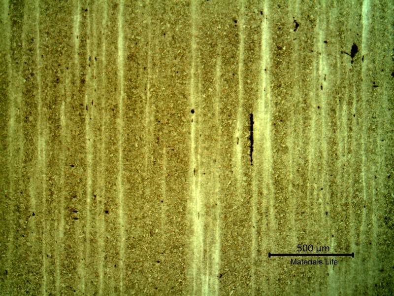 Low magnification micrography presenting segregation bands in a martensitic structure. In the segregated regions the Nital etch effect is lower and the bands appear lighter.  The black spots and lines are inclusions (some elongated) in the band.