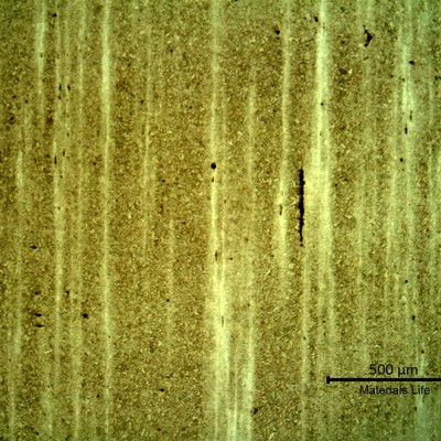 Low magnification micrography presenting segregation bands in a martensitic structure. In the segregated regions the Nital etch effect is lower and the bands appear lighter. The black spots and lines are inclusions (some elongated) in the band.