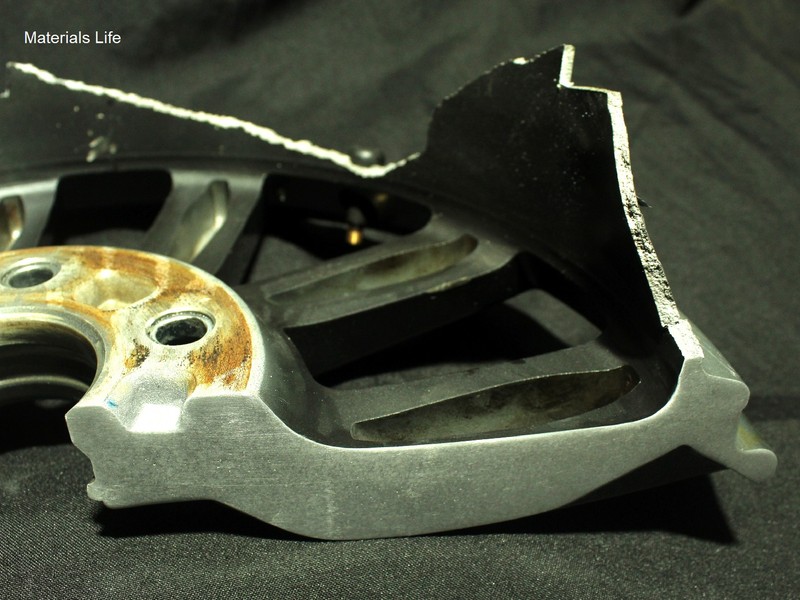 Macro view of a fractured wheel spoke section showing an irregular, shear-lip fracture edge consistent with ductile overload.