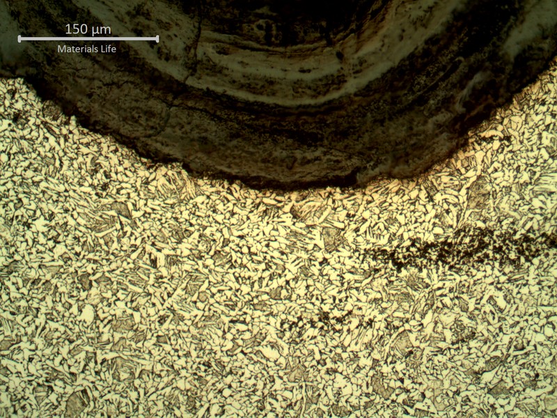Cross-section near a threaded surface showing an acicular matrix structure bordered by a dark, layered corrosion/oxide band along the thread root.