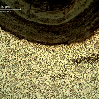 Cross-section near a threaded surface showing an acicular matrix structure bordered by a dark, layered corrosion/oxide band along the thread root.